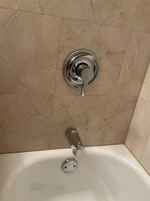 Responded to service call for recurring bathtub faucet drip and ceiling moisture concerns. Inspected chrome shower valve assembly and tub spout in tiled alcove bathtub installation. Assessed two areas of ceiling with visible water staining to identify potential leak sources above bathroom fixtures. Brought ladder for overhead access and replacement faucet components as requested due to ongoing issue requiring third visit.