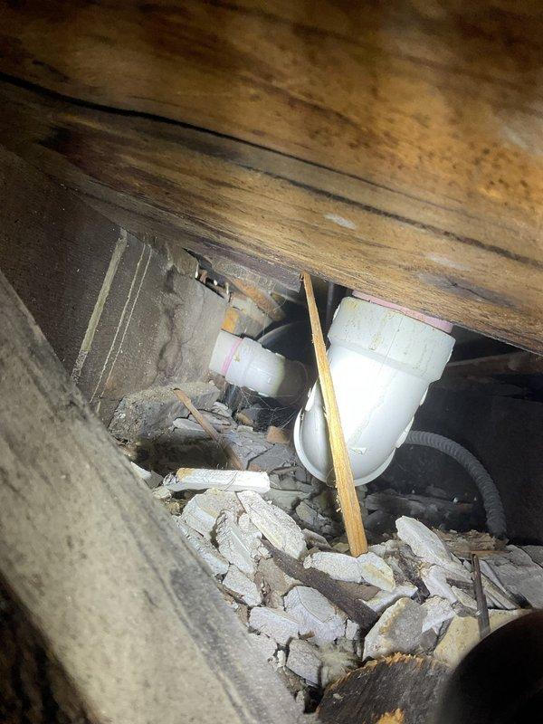 Responded to priority service call for water leak manifesting in ceiling of residential property. Conducted thorough investigation of affected area, including visual inspection of ceiling penetration points and architectural features in high-ceiling space. Accessed crawl space beneath flooring to locate source of water intrusion. Identified plumbing system components in subfloor area with drainage aggregate present. Documented conditions of wooden floor joists showing moisture staining and discoloration, concrete block foundation wall, and PVC plumbing infrastructure. Photographed evidence of leak location and surrounding structural elements for repair assessment.