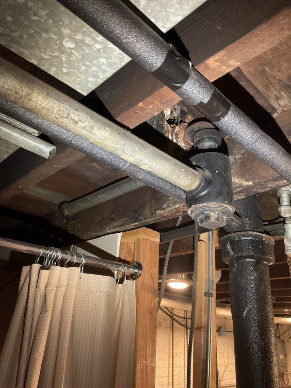 Responded to service call for slow-draining bathtub and second-floor bathroom backup with sewer odor. Conducted inspection of basement plumbing infrastructure, documenting exposed drainage lines, pipe connections, and overall condition of the waste system beneath the affected areas. Photographed visible plumbing configuration including horizontal drain runs, vertical stacks, pipe fittings, and support systems to assess potential blockage points and ventilation issues causing the drainage problems and odor complaints.