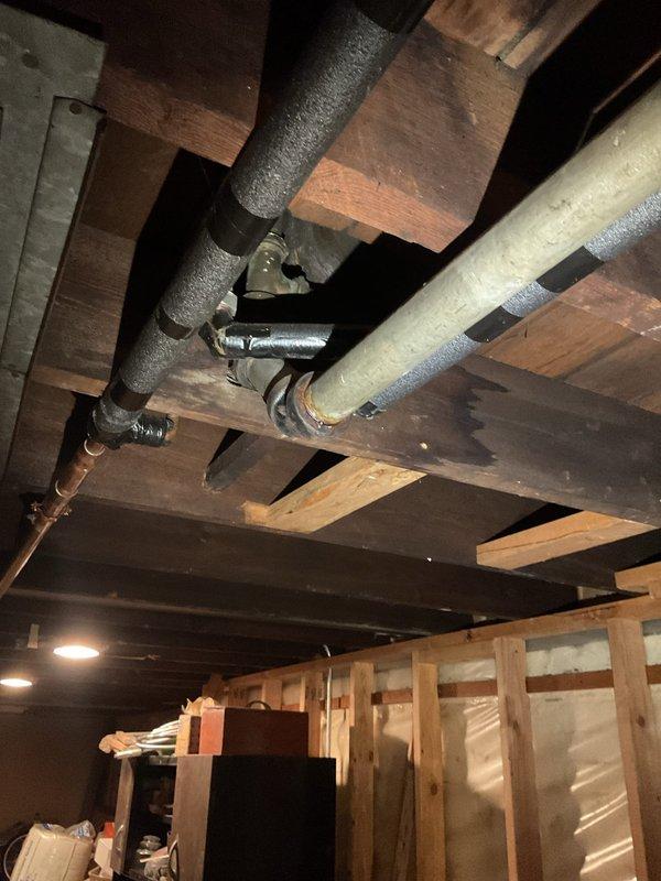 Responded to service call for slow-draining bathtub and second-floor bathroom backup with sewer odor. Conducted inspection of basement plumbing infrastructure, documenting exposed drainage lines, pipe connections, and overall condition of the waste system beneath the affected areas. Photographed visible plumbing configuration including horizontal drain runs, vertical stacks, pipe fittings, and support systems to assess potential blockage points and ventilation issues causing the drainage problems and odor complaints.