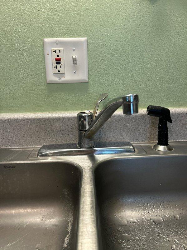 Replaced existing kitchen faucet with new unit per customer request. Removed old chrome faucet assembly from center-mounted position on stainless steel double-basin sink, disconnected supply lines, and installed new faucet with single lever handle and coordinating black spray nozzle attachment. Verified proper water flow, tested for leaks at all connections, and confirmed full functionality of both main faucet and spray attachment.
