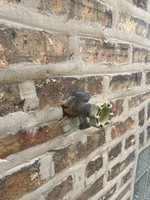 # Outdoor Spigot Repair and Leak Investigation

Responded to service call for exterior hose bib evaluation on brick structure. Upon inspection, identified aging brass spigot with visible oxidation and patina buildup on valve body and mounting hardware. Cross-handle showed wear consistent with extended use.

Investigation revealed active water intrusion affecting interior attic space directly behind spigot mounting location. Traced leak path from exterior wall penetration through brick mortar joint into crawl space area. Documented extensive moisture damage to insulation material with characteristic yellowish-brown staining and discoloration concentrated around the supply line entry point. Copper supply piping showed signs of condensation and potential joint failure at wall transition.

Assessed compromised insulation integrity and water-damaged materials in affected attic section. Identified need for spigot replacement, supply line repair at wall penetration, and proper sealing of exte