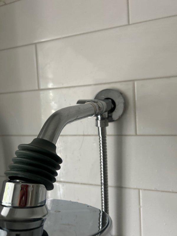 Installed customer-supplied bathroom shower fixtures on white subway-tiled wall. Mounted chrome shower head with rain-style spray pattern on wall arm with black rubber coupling boot, installed handheld shower wand holder with flexible braided stainless steel hose, and secured chrome tub spout with escutcheon plate and drain chain assembly. All fixtures properly sealed and tested for proper operation and water flow.