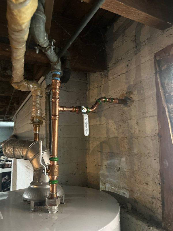 Conducted comprehensive assessment of residential plumbing system for complete home repipe estimate. Evaluated existing copper piping infrastructure throughout property, including main water supply lines, distribution piping, and fixture connections. Inspected basement mechanical room where main water service enters the building, documenting current copper pipe configuration, shutoff valves, and water heater connections with green O-ring gaskets at junction points. Assessed bathroom plumbing serving pedestal sink with chrome fixtures and toilet, examining supply lines and drain connections behind finished tile walls and checkered floor. Photographed existing piping conditions, valve placements, and access points to determine scope of work required for full residential repipe project. Identified routing requirements through basement joists and wall cavities to minimize disruption during future installation.