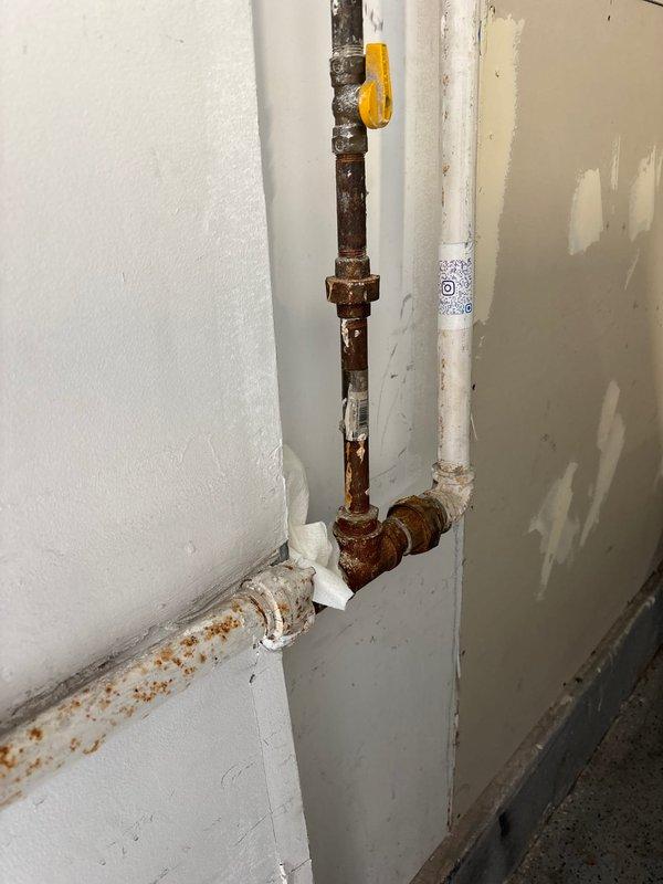 Responded to gas leak call near meter location. Upon inspection, identified active gas leak in heavily corroded piping system at exterior meter connection point. Copper piping exhibited significant weathering and oxidation with brownish-red patina throughout multiple joints and fittings. Interior gas piping showed extensive rust corrosion on vertical and horizontal runs, with deteriorated conditions present on brown pipe sections and fittings near gas shutoff valve. Documented conditions with photographs showing compromised pipe integrity at multiple connection points including 90-degree elbows and solder joints. Recommended complete replacement of corroded gas piping system due to safety concerns and extent of deterioration. Provided estimate for necessary repairs to eliminate leak hazard and restore system to code compliance.