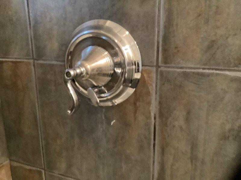 Completed installation of chrome-finished single-handle shower mixing valve with circular escutcheon plate and lever-style control handle on tiled wall surface. Building water supply was shut down at 9am to facilitate the fixture installation. Also installed wall-mounted plumbing connections near toilet fixture, with two metallic valve assemblies mounted on bathroom wall.