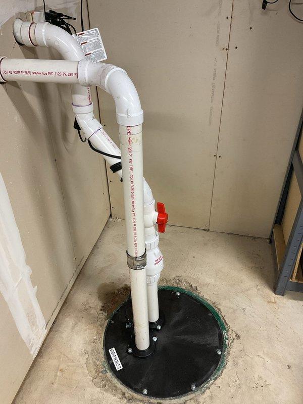 Completed commercial drain and sewer estimate for a facility undergoing interior construction. Assessed and documented the installation of a sump pump system with PVC discharge piping, including a floor-mounted pump pit with cover, vertical discharge line with multiple 90-degree elbows, and a red ball valve for system isolation. Evaluated the electrical connections and control unit mounted to wall framing for the pump operation. The system was designed to manage groundwater or drainage in the below-grade or utility area of the commercial space.