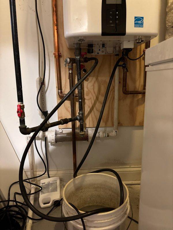 Performed camera inspection of tankless water heater installation and associated plumbing connections in utility closet. Documented wall-mounted Energy Star certified unit with copper supply lines, white PEX piping, black flexible gas lines, and multiple shut-off valves including red-handled isolation valve. Photographed complete system configuration mounted on plywood backing, capturing all pipe routing, fittings, and connections for service records.