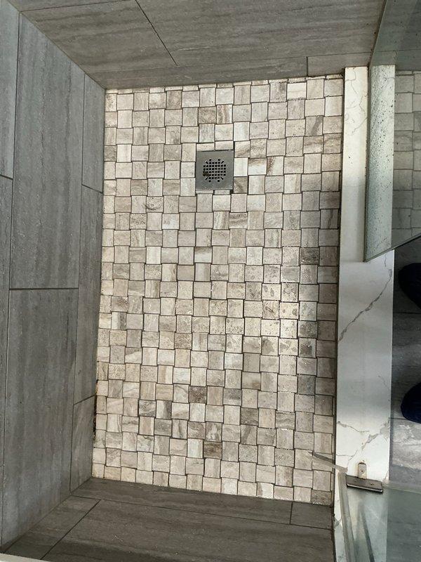 Responded to report of slow water leak from shower penetrating into unit below. Conducted thorough inspection of shower enclosure with natural stone mosaic tile flooring and wood-grain porcelain wall tiles. Identified compromised waterproofing system allowing water migration through substrate. Documented existing tile installation and drain assembly configuration to determine source of water intrusion affecting lower level unit.