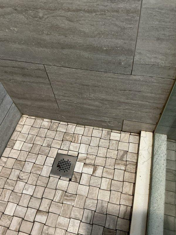 Responded to report of slow water leak from shower penetrating into unit below. Conducted thorough inspection of shower enclosure with natural stone mosaic tile flooring and wood-grain porcelain wall tiles. Identified compromised waterproofing system allowing water migration through substrate. Documented existing tile installation and drain assembly configuration to determine source of water intrusion affecting lower level unit.