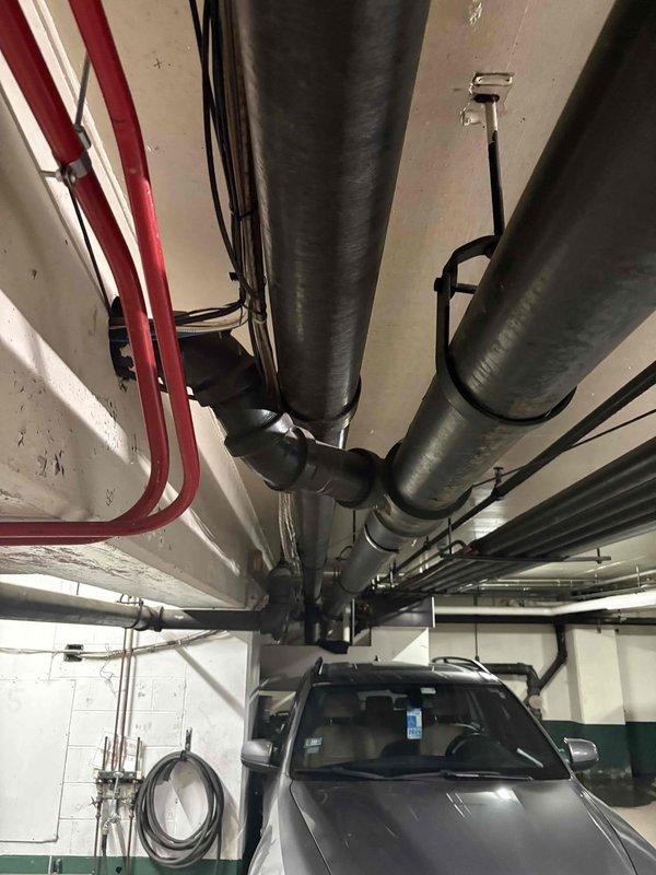 Conducted comprehensive walk-through of commercial building mechanical space to assess existing piping infrastructure and develop material list for upcoming installation. Documented overhead ceiling-mounted systems including large-diameter ductwork, insulated pipes, red-painted conduit lines, electrical wiring bundles, and associated mounting hardware and brackets in parking garage area to determine scope of work and required materials for piping installation project.