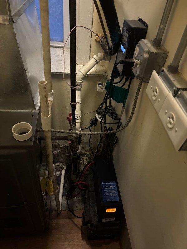 Responded to service call for banging noise originating from sump pump system. Upon arrival, inspected the iOn Technologies 35ACI Battery Backup System and found the unit displaying operational readings but exhibiting signs of potential battery failure. Evaluated the complete sump pump installation including primary pump, discharge piping, check valve assembly, and backup power system. Discussed with property owner the comparative benefits and longevity expectations between full system replacement versus component-level repair of the battery backup unit. Documented existing equipment configuration including PVC discharge lines, electrical connections, and control panel setup through photographic records for reference and future maintenance planning.