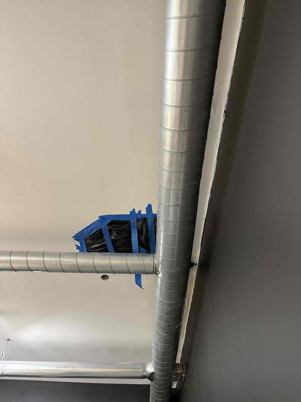 Responded to leak investigation request in common area. Conducted thorough assessment to locate source of water intrusion. Inspection revealed moisture issue requiring access through wall cavity. Installed temporary containment measures including plastic sheeting secured with painter's tape over wall opening to prevent debris spread during investigation. Documented HVAC ductwork configuration and junction points in affected area, noting blue tape marking at duct connection that may indicate previous repair attempt or current leak source. Investigation focused on determining whether leak originated from plumbing system or HVAC condensate drainage. Photographed conditions for record and recommended next steps for permanent repair once leak source is confirmed.