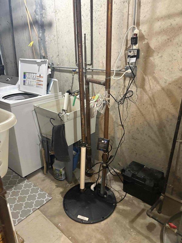 Responded to report of sump pump leaking when washing machine drains. Inspected sump pump system, discharge piping, and battery backup unit in basement utility area. Evaluated washing machine drain connection to identify source of water intrusion into sump basin. Assessed condition of existing battery backup system and verified proper operation of pump float switch and check valve assembly.