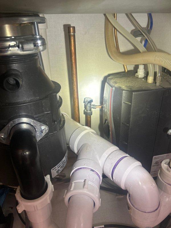 Installed customer-supplied water treatment system under kitchen sink, integrating the filtration unit with existing plumbing configuration that includes garbage disposal, copper supply lines, and PVC drain assembly. Connected system to cold water supply line and verified proper operation of all components including disposal, P-trap drainage, and new filtration unit with flexible discharge line.