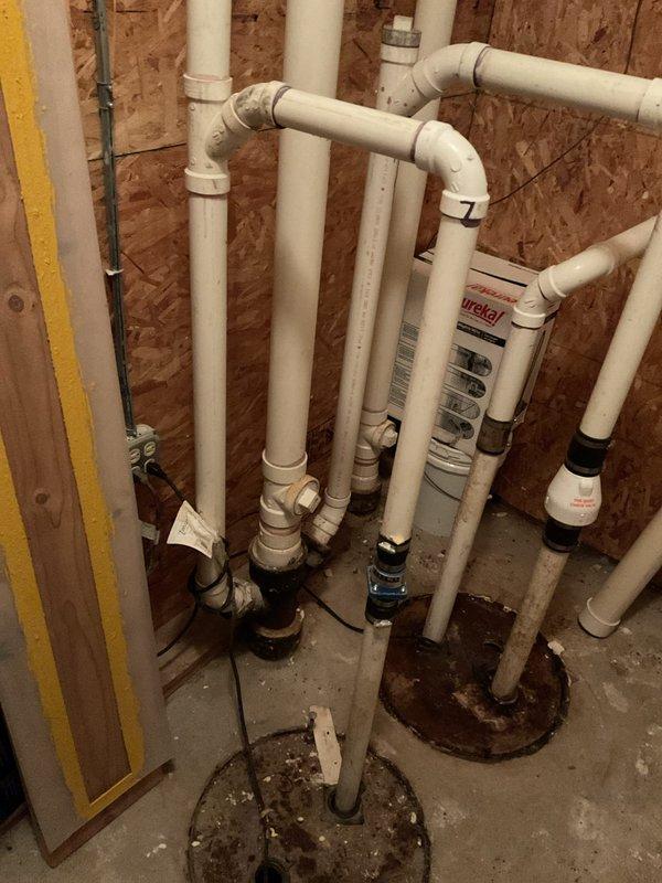 Completed catch basin cleaning and ejector pit maintenance at residential property. Serviced floor drain system with rusted metal collar and removed accumulated sediment and debris from pit containing standing water. Performed routine maintenance on ejector pit system connected to white PVC plumbing infrastructure in unfinished basement area. Inspected multiple corroded floor flanges at pipe penetrations through concrete slab and verified proper drainage function. System operational upon completion with all drainage pathways clear.
