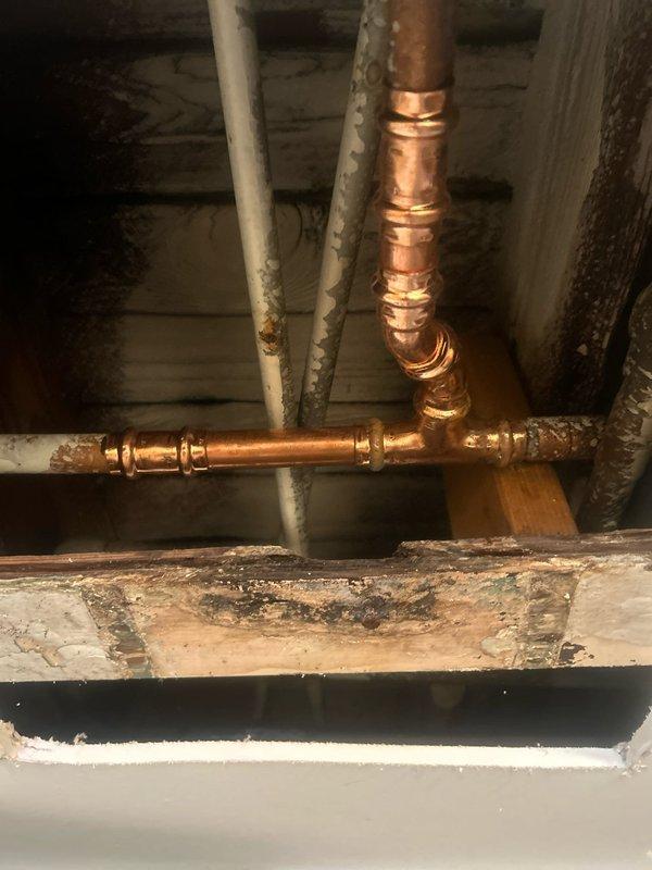 Responded to water leak investigation in basement bathroom area. Located active leak at soldered copper pipe joint connection on vertical riser serving bathroom fixtures. Inspected surrounding copper supply lines, fittings, and solder joints in crawl space area beneath bathroom. Documented condition of plumbing system including copper piping with visible oxidation, galvanized steel lines with shut-off valve, and mixed plumbing infrastructure. Identified failed solder joint as source of water intrusion. Photographed leak location and affected plumbing components for repair estimate documentation.