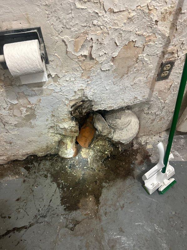 Conducted on-site assessment of bathroom plumbing system with non-compliant soil pipe requiring code upgrades. Documented extensive water damage, deteriorated wall surfaces with severe paint failure, and active moisture intrusion around existing copper and white piping penetrations at floor level. Identified significant mold growth, structural decay, and compromised substrate conditions throughout lower wall sections and concrete flooring. Prepared comprehensive estimate for soil pipe replacement and code compliance work, including necessary repairs to damaged surrounding surfaces and remediation of water-affected areas.