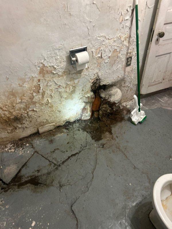 Conducted on-site assessment of bathroom plumbing system with non-compliant soil pipe requiring code upgrades. Documented extensive water damage, deteriorated wall surfaces with severe paint failure, and active moisture intrusion around existing copper and white piping penetrations at floor level. Identified significant mold growth, structural decay, and compromised substrate conditions throughout lower wall sections and concrete flooring. Prepared comprehensive estimate for soil pipe replacement and code compliance work, including necessary repairs to damaged surrounding surfaces and remediation of water-affected areas.