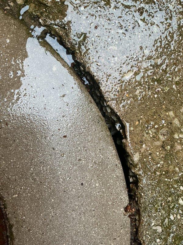 Responded to emergency service call for deteriorating catch basin showing structural failure. Upon inspection, found catch basin cover embedded in damaged concrete floor with significant surface deterioration, cracking, and water damage evident throughout surrounding area. Exterior assessment revealed severe structural compromise with irregular cracks, heavy moss and algae growth indicating chronic moisture infiltration, and complete deterioration of adjacent surfaces. Documented extensive damage to both interior and exterior catch basin components requiring full replacement due to caving conditions and safety concerns.