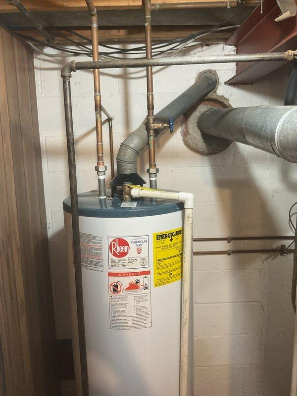 Provided comprehensive estimate for preemptive replacement of existing Rheem 50-gallon tall gas water heater with new Rheem Performance 50-gallon tall gas water heater in basement of home constructed in 1967-1969. Estimate includes complete removal and disposal of existing unit, installation of new water heater with all necessary copper piping connections, shut-off valves, and gas line hookup, plus all required materials, labor, permits, and full compliance with municipal code requirements and inspection. Current installation shows standard residential configuration with copper supply lines, appropriate venting through existing ductwork, and connections to overhead plumbing system in unfinished basement utility area.
