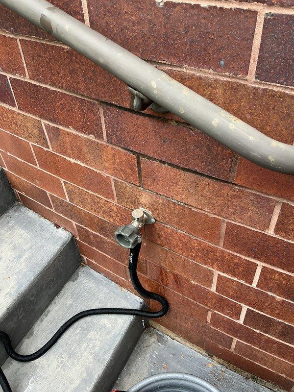 Responded to service call for multiple plumbing issues including dripping shower in master bathroom, leaking outdoor hose bibs, and noisy upstairs toilet. Inspected both exterior spigots mounted on brick wall and identified leaking at hose connection points when hoses were attached. Assessed hose bib washers and connection threads for wear and proper sealing. Evaluated master bathroom shower valve for internal component failure causing drip. Examined upstairs toilet flush mechanism to diagnose source of unusual noise during flush cycle. Documented exterior plumbing fixtures with photographic evidence showing hose bib installations, attached garden hoses, and mounting conditions on brick exterior walls.