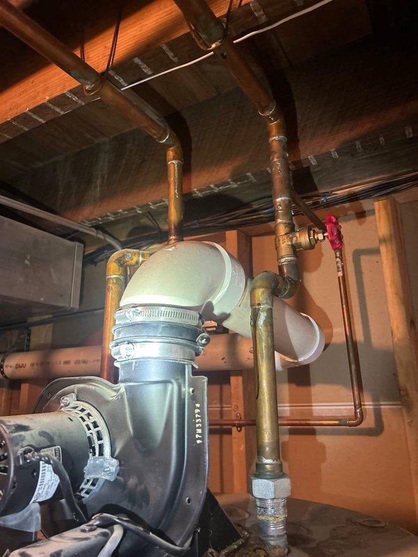 Responded to service call for water heater leaking from top with no hot water available. Upon inspection, found aging water heater installed in 2008 showing signs of deterioration at top connections. Observed corroded copper piping with significant oxidation and patina formation throughout the plumbing system. Documented existing infrastructure including brass valves with red handles, PVC drainage piping, and basement mechanical installation. Assessed condition of water heater connections, supply lines, and associated plumbing components to provide comprehensive estimate for water heater replacement and necessary piping modifications.