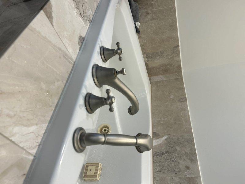 Completed installation of new bathtub and shower fixtures in master bathroom, including three cross-handle valves with brushed nickel finish, tub spout, and handheld shower head assembly mounted to tub deck. Addressed previous cold water leak on master bathroom tub by replacing faulty valve components and ensuring proper seating and seal integrity. Installed widespread bathroom sink faucet with traditional cross-handle design in brushed nickel finish, replacing previous fixture and repairing leaking kitchen sink trap with new P-trap assembly and proper compression fittings. All fixtures tested for proper operation and leak-free performance upon completion.