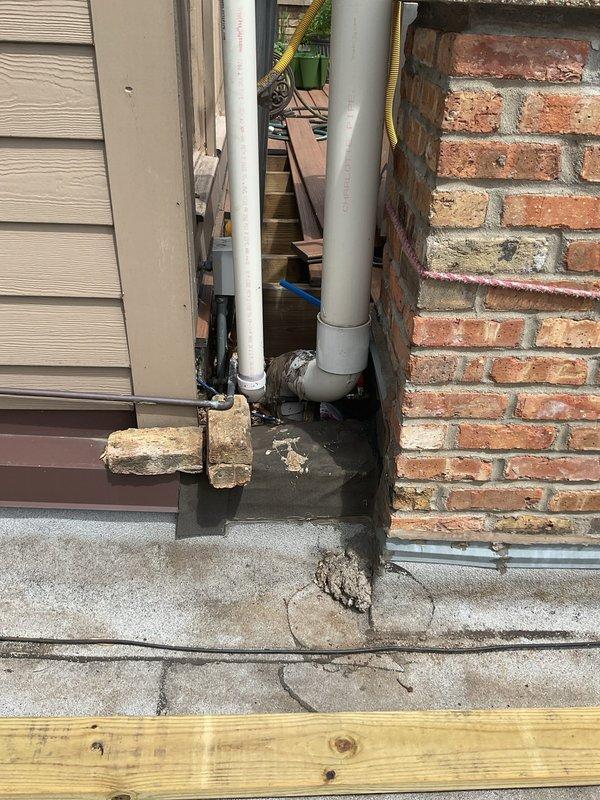 Responded to service call for slow draining bathtub and burst rooftop deck water service line. Assessed the rooftop deck plumbing system and identified failed water service line requiring complete replacement. Replaced compromised exterior water supply piping with new PVC pipe assembly, including proper fitting connections and vertical to horizontal transitions at building corner where brick wall meets siding. Addressed drainage issues in bathtub to restore proper flow. Documented existing conditions showing water damage and deterioration at pipe connection points on foundation surface prior to repairs.