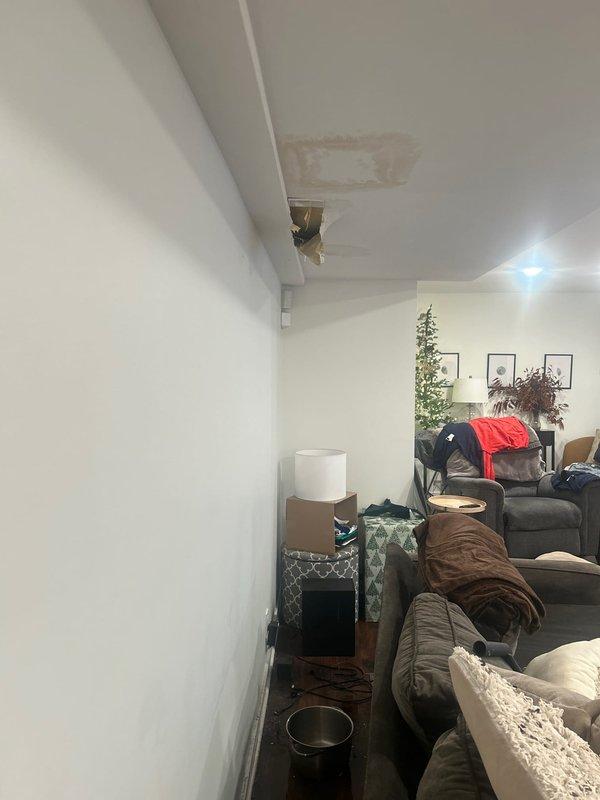 Performed water leak location service at residential property. Investigation revealed active water intrusion in main living area ceiling with visible brownish water staining and compromised drywall requiring access opening. Traced moisture source from upper level plumbing system affecting ceiling structure and identified leak origin point. Documented damage extent in both primary living space and basement level areas for repair recommendations.