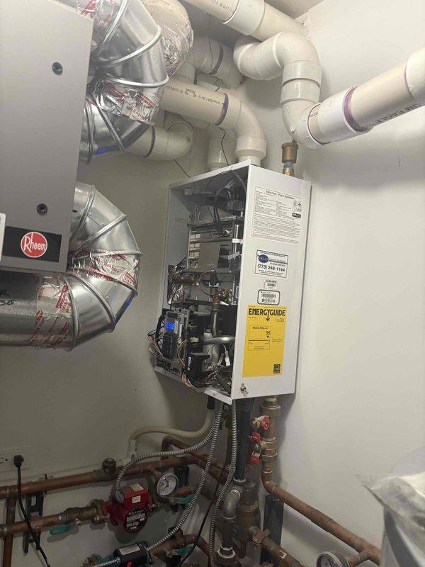 Completed installation and commissioning of a multi-zone hydronic heating system featuring a wall-mounted tankless water heater with integrated boiler functionality. The system includes an extensive copper piping network with multiple circulation pumps, turquoise ball valves, and red-handled isolation valves for zone control. Installed pressure gauges and monitoring equipment throughout the assembly to ensure proper system performance. Configured PEX tubing runs for distribution, secured all piping with appropriate mounting brackets, and completed electrical connections including power supply to circulation pumps. Routed metallic flexible conduit for electrical protection and installed silver insulated ductwork with PVC venting system. All components tested and verified operational with proper pressure readings confirmed.