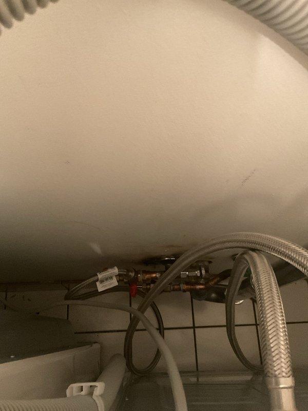 Responded to service call for washer not receiving hot water at 50-year-old condominium unit. Upon inspection, assessed water heater connections and supply line configuration in utility closet. Examined existing shutoff valves, flex lines, and plumbing connections at water heater to diagnose hot water supply issue affecting washing machine. Documented installation with photos showing water heater underside, brass fittings, braided stainless steel flex lines, and valve assembly for service records and potential repair recommendations.