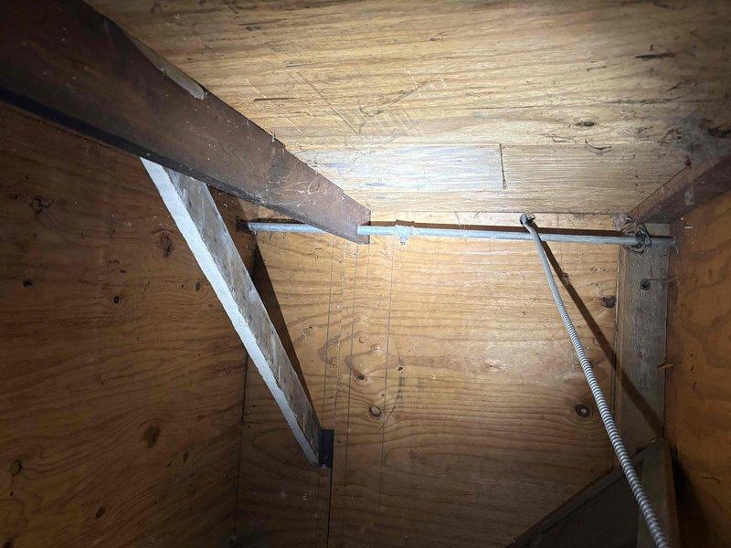 Responded to a priority call for a non-functional exterior plumbing connection that had been inoperative for approximately six months at a century-old residence. Upon inspection, accessed the crawl space and vertical utility chase to assess the damaged piping system. Found severely corroded copper piping with extensive oxidation and greenish-brown patina throughout the affected section, indicating prolonged exposure and deterioration. The compromised pipe showed threaded connections with visible corrosion at junction points and a white elbow fitting. Evaluated the routing of the existing plumbing line through the structural framing members and documented the condition of the installation for repair planning. Photographed the corroded copper pipe, deteriorated fittings, and surrounding structural components including wooden framing, insulation, and the vertical service corridor to provide a complete assessment of the repair scope required to restore functionality to the exterior water c