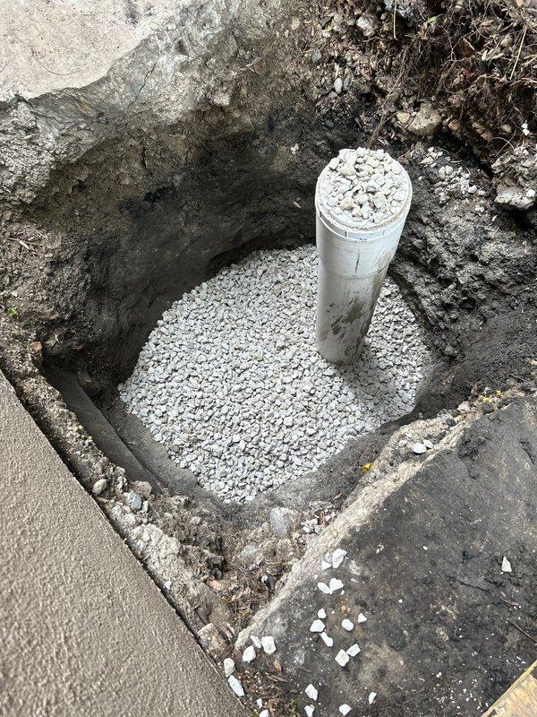 Completed main line sewer installation involving excavation and installation of new PVC drainage system. Excavated trench alongside building foundation, installed 4-6 inch diameter PVC pipe with proper gravel bedding and drainage column for structural support and water management. Routed additional PVC piping through drainage channel adjacent to brick wall foundation, ensuring proper pitch and alignment for optimal flow. Backfill and compaction to be completed upon final inspection.