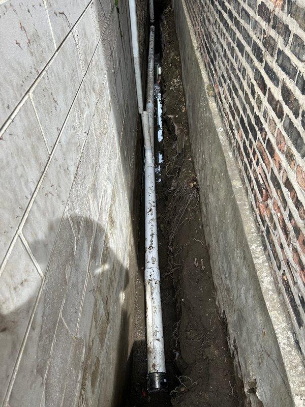 Completed main line sewer installation involving excavation and installation of new PVC drainage system. Excavated trench alongside building foundation, installed 4-6 inch diameter PVC pipe with proper gravel bedding and drainage column for structural support and water management. Routed additional PVC piping through drainage channel adjacent to brick wall foundation, ensuring proper pitch and alignment for optimal flow. Backfill and compaction to be completed upon final inspection.