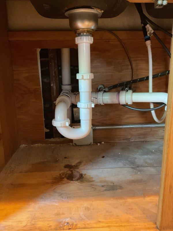 Completed full kitchen stack replacement due to severe grease and sludge accumulation in existing drainage system. Performed demolition of kitchen cabinetry to access galvanized tee fitting and vent piping. Removed all existing kitchen drainage components and adapted connections to existing vent system. Cut down 3" clay tile at floor level using grinder to establish band connection, then converted system to PVC and reduced to 2" diameter. Rodded drainage line to catch basin while piping remained exposed to ensure clear flow path.

Installed approximately 15 feet of 2" PVC drain line with new 2" cleanout access point for future maintenance requirements. Reduced pipe diameter to 1½" prior to vertical stack installation. Installed new tee connection in vertical run and added wye fitting to separately pipe and trap dual sink basins. Replaced basket strainers in both sink compartments with new units and installed tubular drain piping. Added new dishwasher tailpiece and adapted all connectio