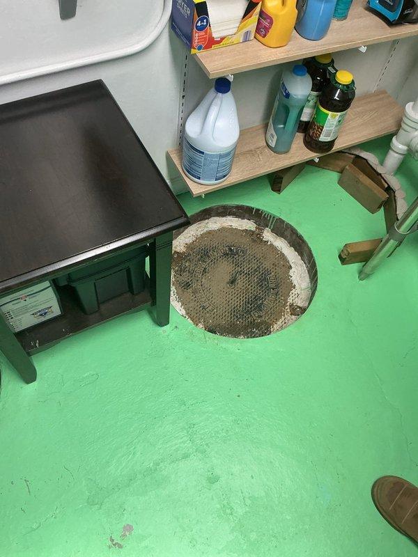 Responded to afternoon appointment for catch basin cover assessment and service. Upon arrival, accessed utility room where sump pump basin was located in floor with bright green painted surface. Inspected existing catch basin installation featuring rusted metal rim and dual white PVC pipe configuration with quiet check valve system. Basin contained operational sump pump mechanism with electrical connections and showed signs of age-related corrosion on metal components. Documented current condition of installation including water level, pipe positioning, and overall basin integrity for maintenance records.