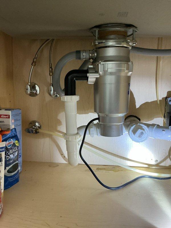 Responded to water leak investigation concerning moisture ring around ceiling light fixture. Performed thorough inspection of kitchen sink plumbing system, including garbage disposal unit, P-trap assembly, supply lines, and dishwasher drain connections. Documented plumbing configuration with disposal unit, white PVC drainage piping, flexible braided supply lines, and corrugated dishwasher hose to identify potential leak source causing water damage to ceiling below.