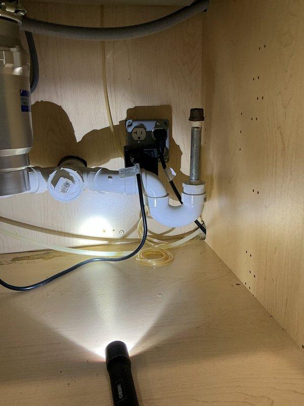 Responded to water leak investigation concerning moisture ring around ceiling light fixture. Performed thorough inspection of kitchen sink plumbing system, including garbage disposal unit, P-trap assembly, supply lines, and dishwasher drain connections. Documented plumbing configuration with disposal unit, white PVC drainage piping, flexible braided supply lines, and corrugated dishwasher hose to identify potential leak source causing water damage to ceiling below.