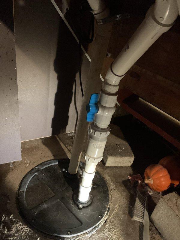 Responded to tenant complaint regarding foul odor emanating from ejector pit and concerns about proper sewage ejection functionality. Upon inspection, identified that the discharge pipe was running warm to the touch, which tenant questioned as abnormal. Assessed the ejector pump system, PVC discharge piping assembly with check valve, and basin conditions to determine operational status and verify proper waste water discharge. Documented existing plumbing infrastructure including vertical discharge line with couplings and valve assembly for service records.