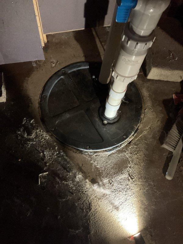 Responded to tenant complaint regarding foul odor emanating from ejector pit and concerns about proper sewage ejection functionality. Upon inspection, identified that the discharge pipe was running warm to the touch, which tenant questioned as abnormal. Assessed the ejector pump system, PVC discharge piping assembly with check valve, and basin conditions to determine operational status and verify proper waste water discharge. Documented existing plumbing infrastructure including vertical discharge line with couplings and valve assembly for service records.