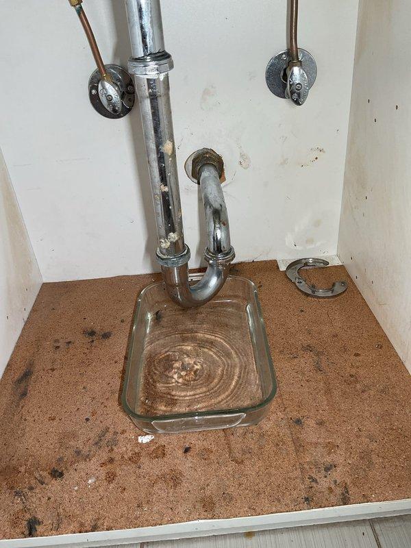 Responded to slow-draining bathroom sink in garden unit of century-old building. Upon arrival, confirmed homeowner had already cleared P-trap without resolving issue, indicating blockage located within wall cavity. Disassembled and inspected P-trap assembly and drain connections under sink to verify proper flow and rule out additional obstructions in accessible plumbing. Placed collection container under drain assembly to catch water during diagnostic work. Documented existing water damage on cabinet floor and evidence of previous leakage. Due to blockage location within wall and age of plumbing system, recommended follow-up assessment with drain camera or potential wall access to locate and clear obstruction in drain line.
