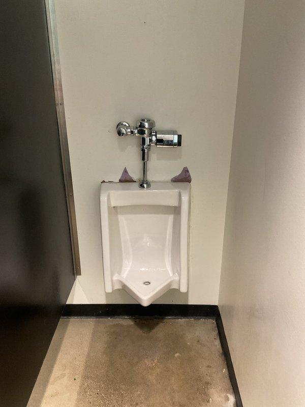 Responded to a commercial men's restroom for a clogged urinal that was not resolved during the initial service visit. Upon inspection, determined that the wall-mounted urinal requires complete removal from the wall to properly address the obstruction. Documented the existing installation, including the flush valve assembly and mounting configuration, and recommended scheduling a follow-up appointment to remove the fixture and clear the blockage.