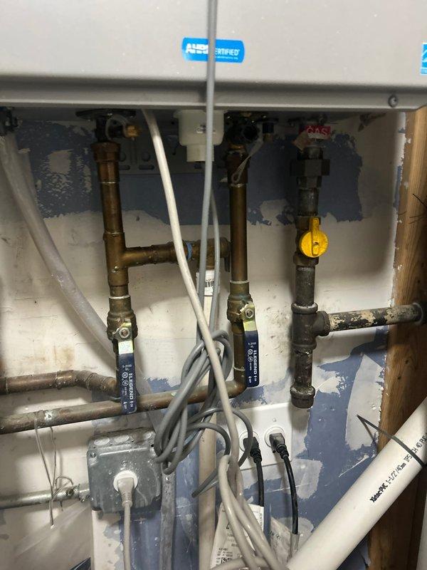 Completed installation and inspection of Rheem Performance Platinum tankless water heater system with associated plumbing connections. Verified proper operation of water supply shut-off valves beneath sink cabinet, documented existing water staining on cabinet interior surfaces, and confirmed temperature settings at 119°F on digital display. All PVC piping connections, inlet/outlet lines, and safety components including pressure relief valve and temperature gauge were inspected and photographed for service records.