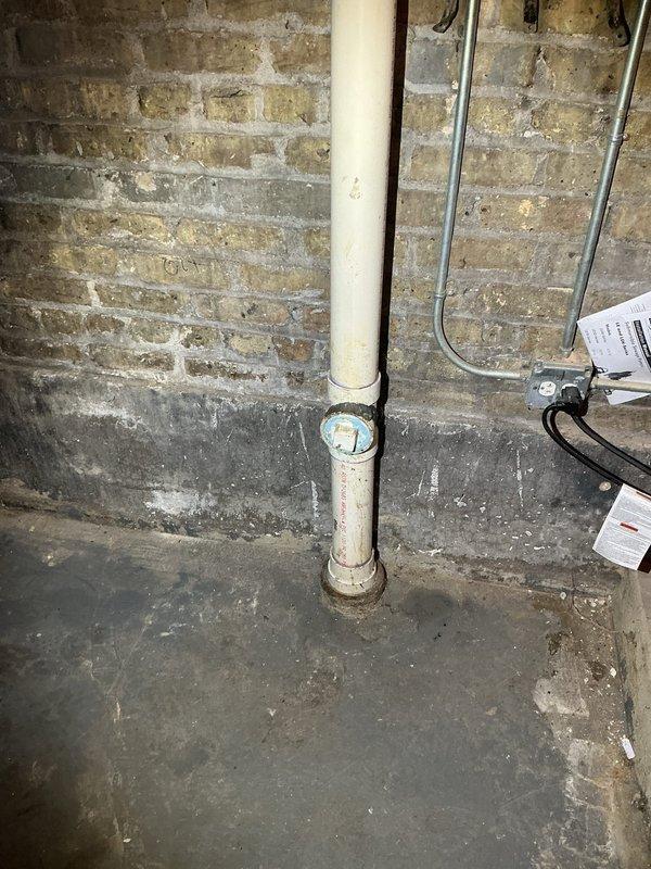 Completed callback to assess cleanout condition and verify scope of previous maintenance service. Upon inspection, documented damaged cleanout fitting on vertical PVC drain line in basement utility area. Photographed the blue-capped cleanout access port showing visible wear and the surrounding plumbing infrastructure including vertical white PVC drainage pipe with manufacturer markings and purple specification bands. Contacted service coordinator to confirm whether hydrojetting was included in prior maintenance visit, as this information is necessary to determine if cleanout damage occurred during previous service or was pre-existing condition.