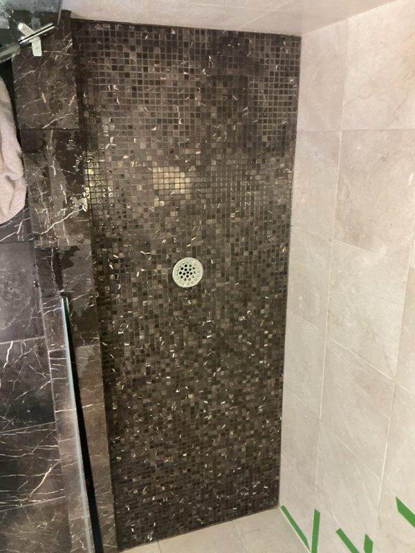 Conducted follow-up site visit to assess shower drain and basement utility area for additional estimate preparation. Documented existing conditions including mosaic tile shower floor with center drain, marble-patterned wall tiles, and basement space showing general wear requiring attention. Photos captured for quality assurance review and estimate development purposes.