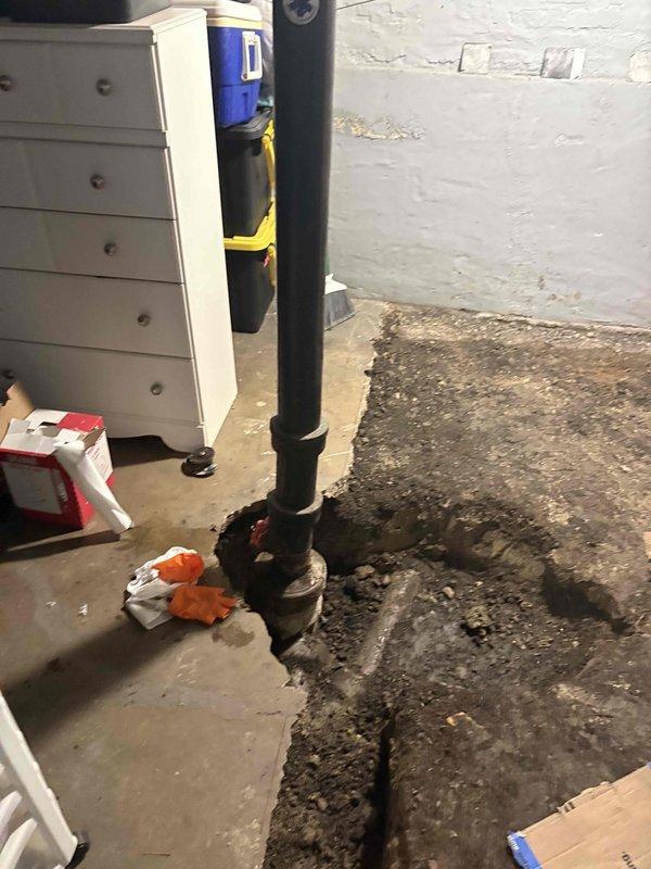 Responded to water leak originating from main plumbing stack. Upon inspection, discovered active leak causing extensive moisture damage to subflooring beneath sink cabinet and concrete basement floor below. The deteriorated P-trap assembly and corrugated drain hose connections showed signs of failure, contributing to water intrusion. Documented existing damage including severely compromised plywood subflooring with advanced peeling and discoloration, as well as substantial water staining on basement concrete floor surrounding the vertical drain stack penetration. Photographed affected areas showing damaged plumbing components, deteriorated flooring materials, and moisture patterns for repair assessment and future remediation planning.