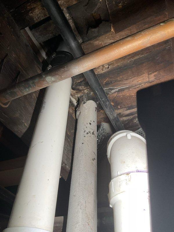 Responded to complaint of intermittent sewer gas odors in 120-year-old residence with suspected vent pipe obstruction. Performed comprehensive inspection of drain-waste-vent system, accessing crawl space to examine plumbing infrastructure including multiple PVC vent stacks and horizontal drain lines. Documented existing conditions showing aged piping with visible weathering and discoloration on vent pipes. Inspected floor joist penetrations and pipe routing to identify potential sources of sewer gas infiltration. Verified proper venting configuration and assessed need for further remediation to resolve ongoing odor issues in the dwelling.