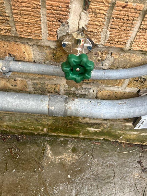 Responded to report of exterior hose bib leaking inside the home. Upon arrival, inspected the outdoor spigot assembly mounted on brick exterior wall and traced water intrusion to failed valve stem packing. The existing galvanized piping showed significant corrosion and weathering consistent with age and outdoor exposure. Disassembled the gate valve assembly, replaced deteriorated packing material and stem washers, reassembled unit, and tested operation under full pressure to confirm leak was eliminated with no interior water penetration.