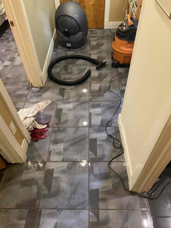 Responded to water intrusion emergency in residential hallway. Deployed wet/dry vacuum and extraction equipment to remove standing water from tile flooring. Assessed sump pump system failure that resulted in basement flooding and water migration to main floor corridor. Utilized commercial-grade water extraction tools and hoses to eliminate pooled water and begin drying process to prevent secondary damage to flooring and baseboards.